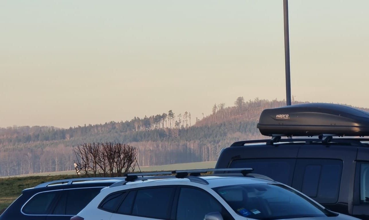 Ein Foto von zwei Autos mit Dachgepäckträgern vor einer Landschaft mit Hügeln und Bäumen.