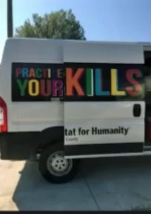 Ein weißer Transporter mit der Aufschrift "PRACTICE YOUR KILLS" in bunten Buchstaben. Darunter steht "Habitat for Humanity".