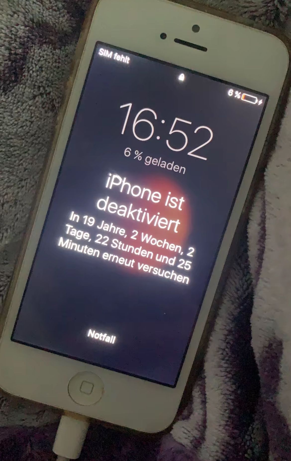 Ein iPhone-Bildschirm zeigt an, dass das iPhone deaktiviert wurde. Es steht "In 19 Jahre, 2 Wochen, 2 Tage, 22 Stunden und 25 Minuten erneut versuchen". Die Uhrzeit ist 16:52 Uhr und der Akkustand 6 %.