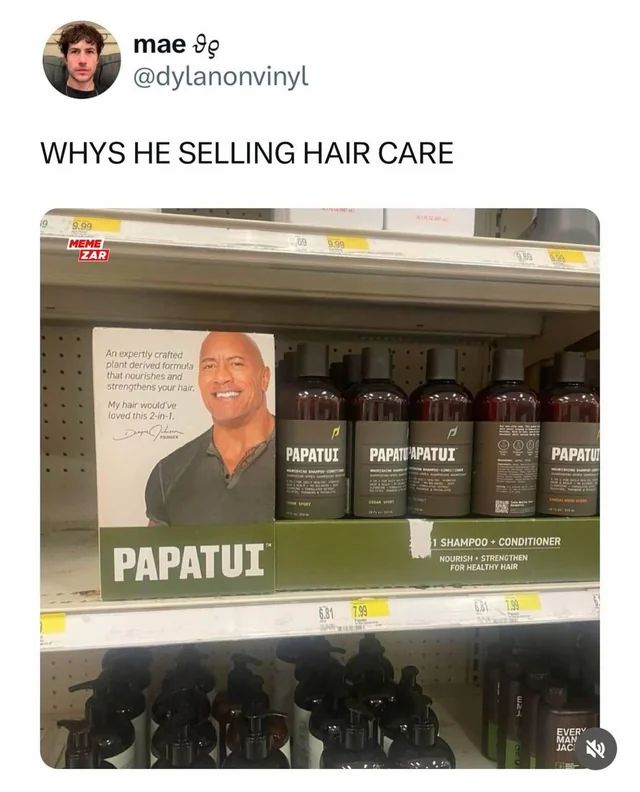 Ein Foto zeigt eine Nahaufnahme von einem Regal in einem Geschäft. Im Regal steht eine Werbeaufsteller für Haarpflegeprodukte mit dem Namen „Papatui“. Der Aufsteller zeigt ein Bild von Dwayne "The Rock" Johnson. Das Produkt wirbt mit einer pflanzlichen Formel, die das Haar nährt und stärkt. Auf dem Regal befinden sich mehrere Flaschen des Produkts. Der Text auf dem Bild lautet: „Warum verkauft er Haarpflege? Eine fachmännisch gefertigte, pflanzliche Formel, die Ihr Haar nährt und stärkt. Mein Haar hätte das geliebt. 2-in-1.“